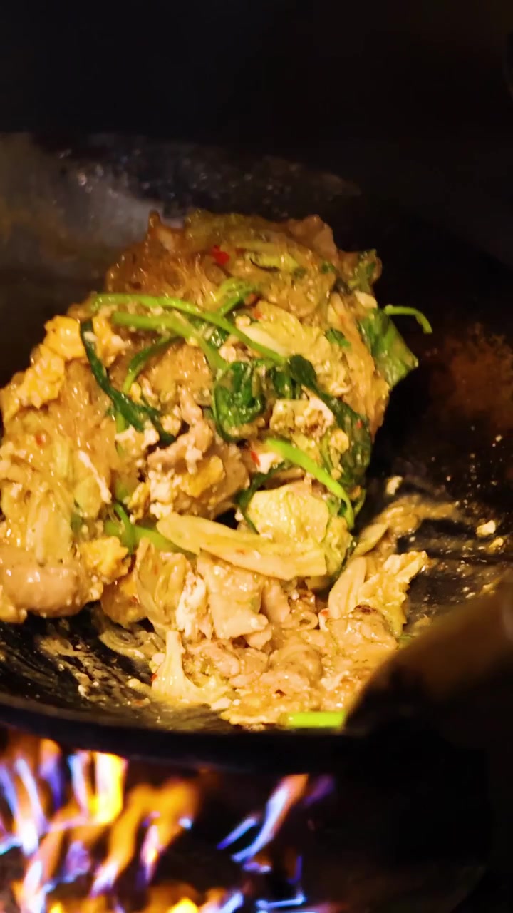 Uno chef salta in padella sukiyaki thailandese con verdure in un wok caldo sotto l'illuminazione notturna.
