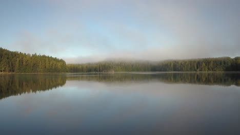 Nube-De-Niebla-Sobre-Los-árboles-Alrededor-Del-Agua-Del-Lago-Con-Reflejo-En-La-Mañana