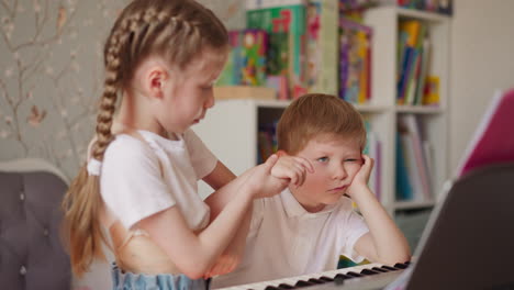 la niña fuerza al hermano menor desinteresado a tocar el piano