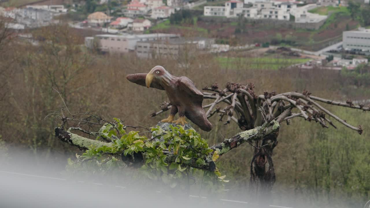 Bird sculpture on a tree with green foliage and a village in background