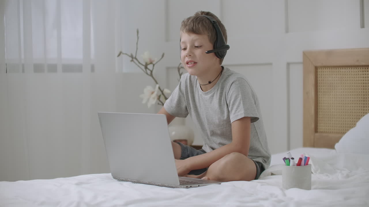 retrato de un niño mirando la pantalla de un portátil y dibujando en un cuaderno escuchando música con auriculares