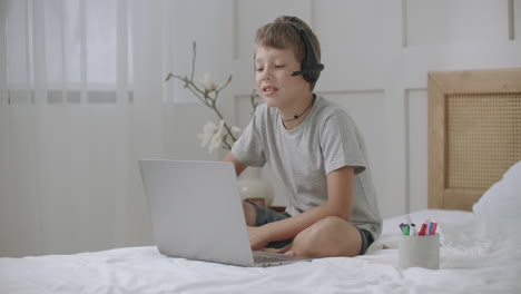 portrait of little boy looking at screen of laptop and drawing at copybook listening music by headphones