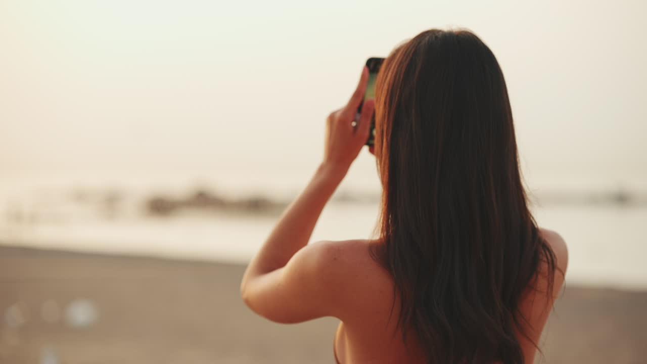 Donna che scatta una foto del tramonto sulla spiaggia
