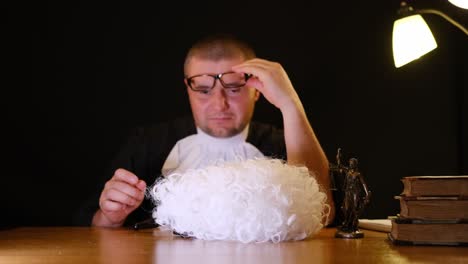 a judge wearing a traditional wig and formal robe firmly holds a gavel at the courtroom table during proceedings