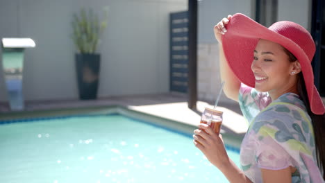 smiling woman in sun hat enjoying drink by swimming pool at home, copy space