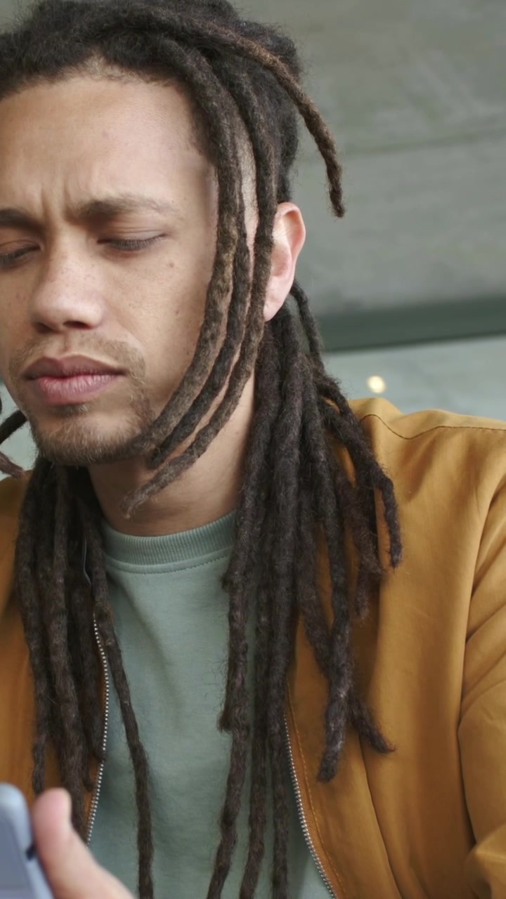 Video verticale: Uomo di mezza età che tocca lo smartphone e legge al caffè, con giacca marrone, smartwatch e anello.
