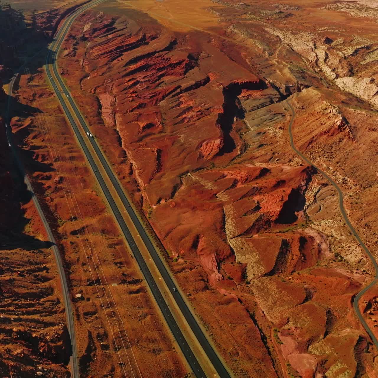 Rocky orange landscape crossed by the motorways with few cars moving by. Stunning scenery of canyons on sunny day from aerial perspective