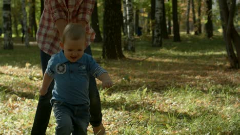 beautiful young mother and her adorable toddler son having fun together in autumn park, boy is running from his mommy