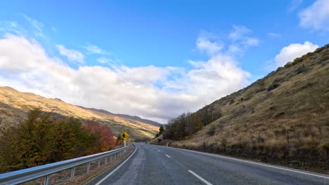a serene drive along a winding road in wanaka, new zealand, with vibrant autumn foliage and clear blue skies
