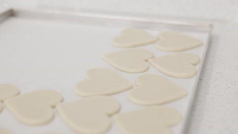 arreglando galletas en forma de corazón recién enrolladas en una bandeja para hornear antes de ponerlas en el horno en una pastelería, cámara lenta de 4k