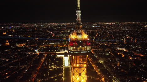 Drone-circling-around-Eiffel-Tower-summit-with-automated-light-beams-sparkling,-Paris-cityscape-and-skylines-at-background,-Aerial-view