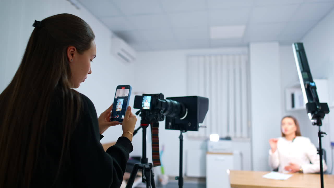 Dark-haired girl takes a video of camera display on the phone. Female blogger creates content for her blog. Blurred backdrop.