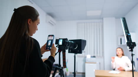 dark-haired girl takes a video of camera display on the phone. female blogger creates content for her blog. blurred backdrop.