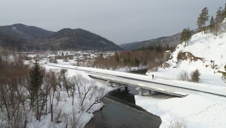 a person walking on a bridge over a river in a snowy landscape