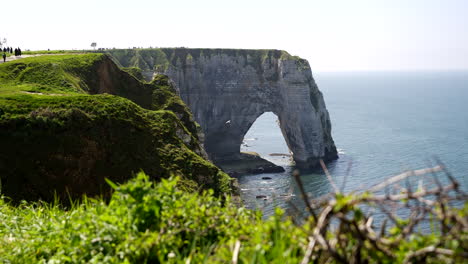 wide shot of famous cliff formation with hole in etrerat and grass in foreground during sunny day - wide shot pedestal shot