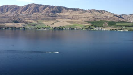 Drone-flying-over-houses-towards-lake-and-mountains