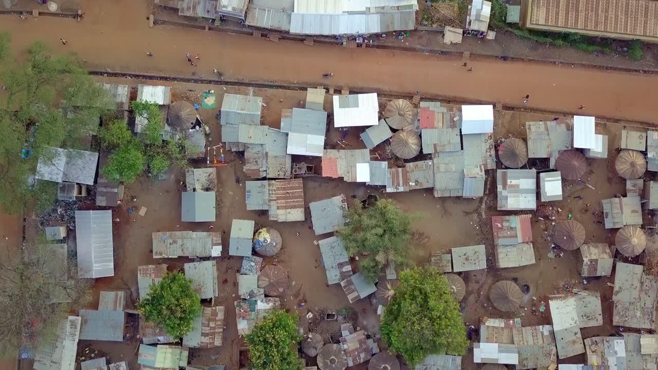 Aerial perspective showcasing densely packed slum housing in Uganda, highlighting corrugated metal roofs and narrow pathways with trees interspersed among the structures, top down drone shot