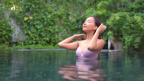 Schöne-Brünette-Asiatische-Frau,-Die-Ihr-Haar-Im-Schwimmbad-Auf-Tropischem-Grünem-Hintergrund-Berührt,-Porträt-zeitlupen-seitenansicht-Bali