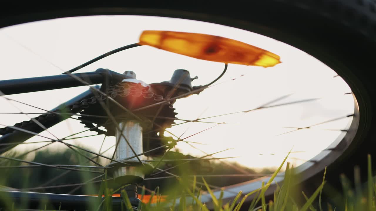 A stunning closeup photograph of a bicycle wheel resting in lush green grass during a magnificent sunset scene