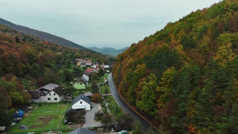 Beautiful-valley-with-village,-autumn-trees,-stream-and-empty-mountain-road-between-the-trees