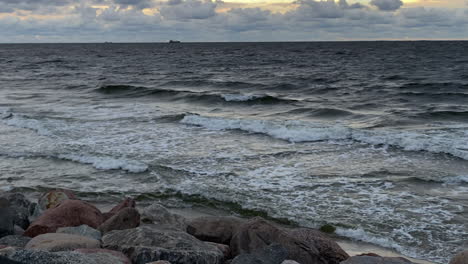 Krachende-Wellen-Durch-Die-Großen-Felsen-Am-Strand-Mit-Vögeln,-Die-Bei-Sonnenuntergang-Unter-Bewölktem-Himmel-Fliegen