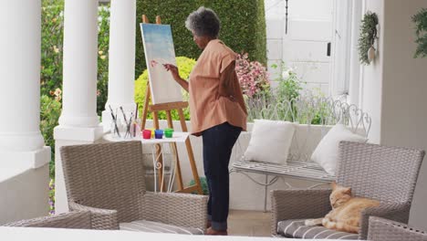 Senior-african-american-woman-painting-while-standing-on-the-porch-of-the-house