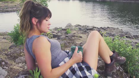 cute hipster girl drinking from a mug and relaxing by the water