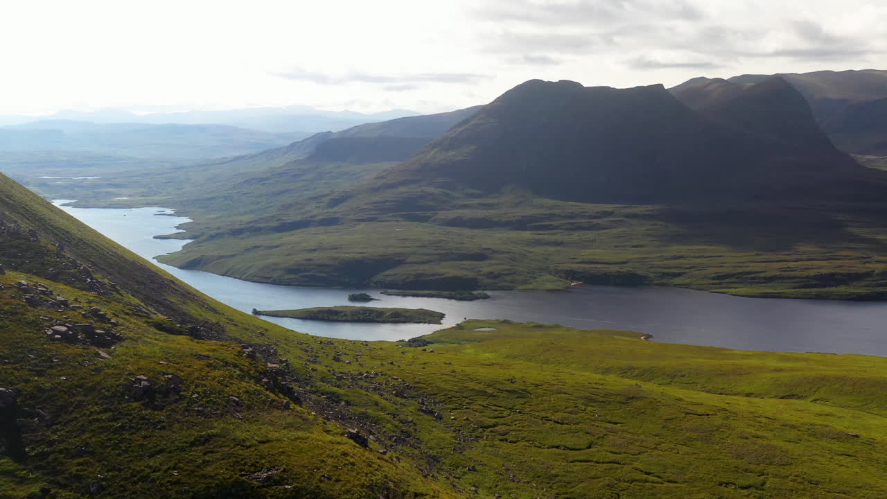 스코틀랜드 북서쪽 고지대에 있는 stac pollaidh의 시네마틱 드론 샷은 바위가 많은 산꼭대기를 지나 멀리 있는 수역으로 이동합니다.