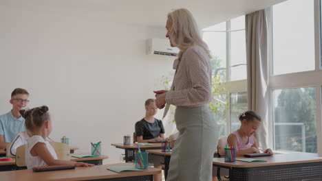 the teacher walks around the classroom of the school. a group of children is sitting at their desks. children write down the task. an elementary school lesson in slow motion. perform control work