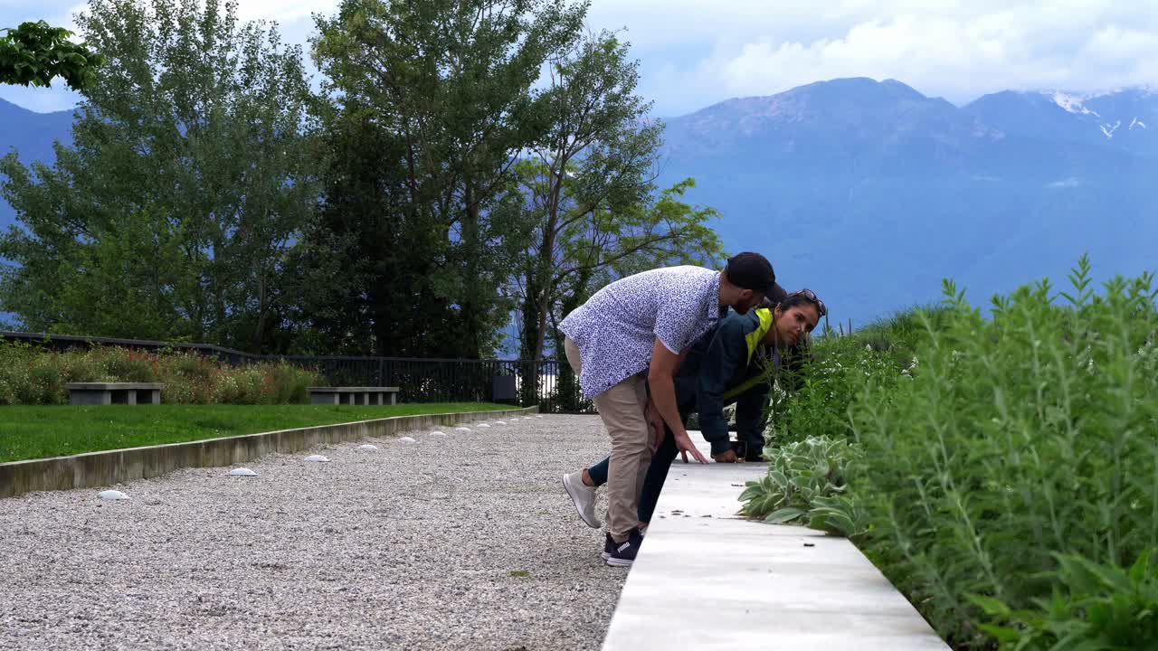 una pareja de viajeros huele a follaje en un parque con fondo de montaña.