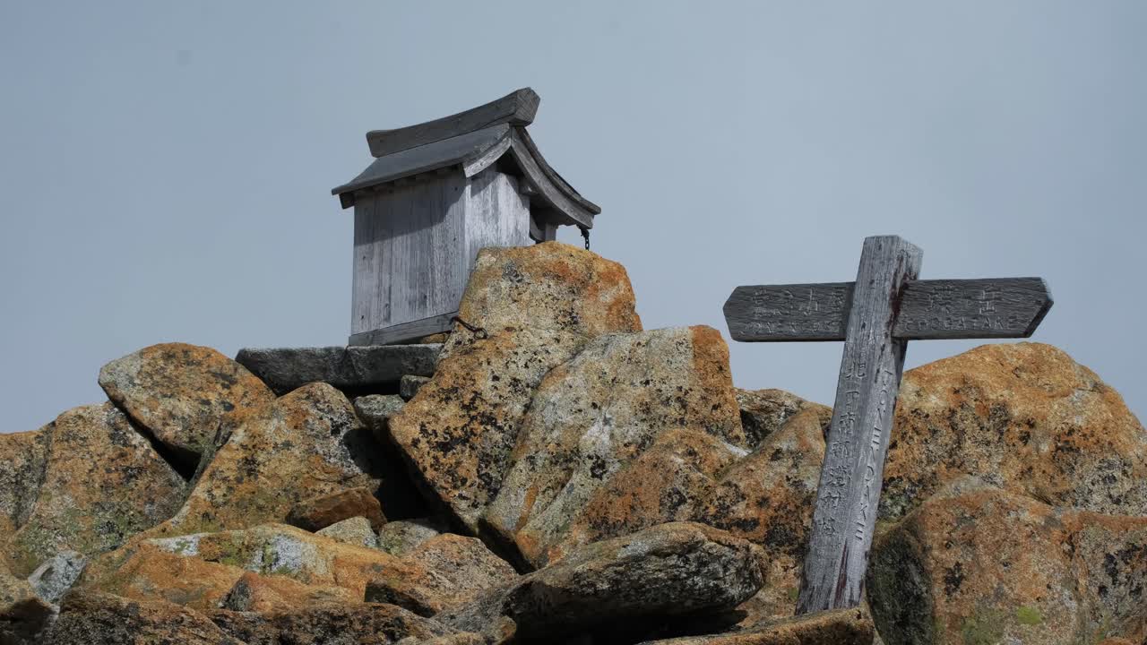 Explore the serene, rocky landscape of Chubusangaku National Park. Capture the rustic charm of a wooden shrine and signpost amid Nagano's rugged mountain scene