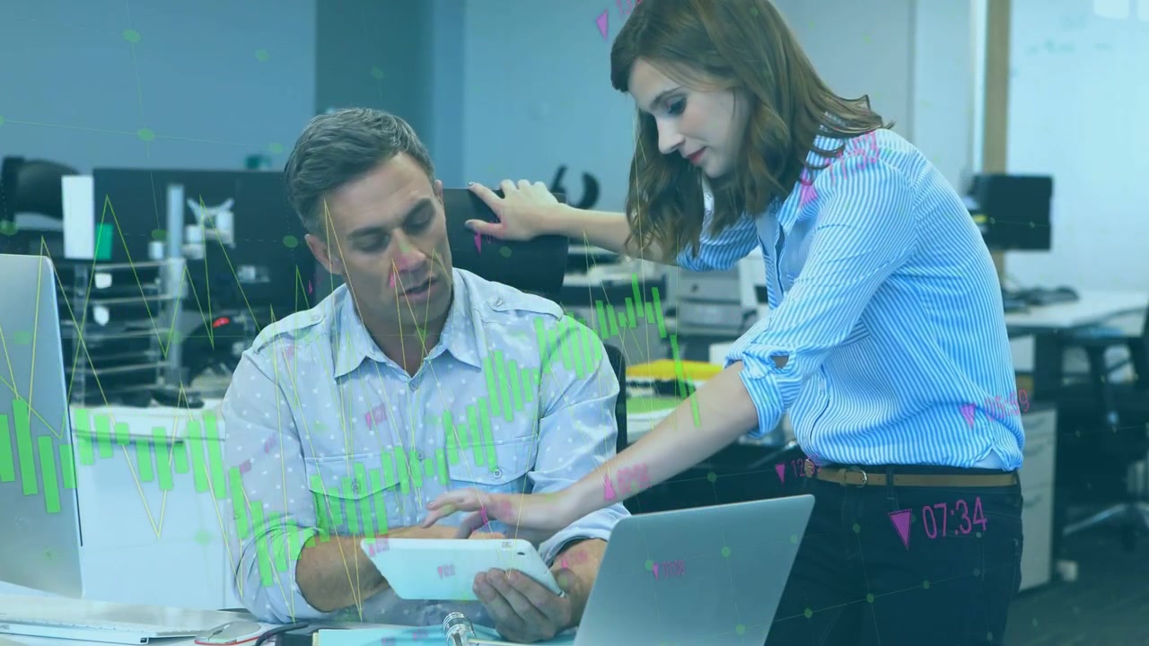 Hombre usando tableta, mujer inclinada y señalando mientras inician una revisión financiera con gráficos superpuestos en la PC