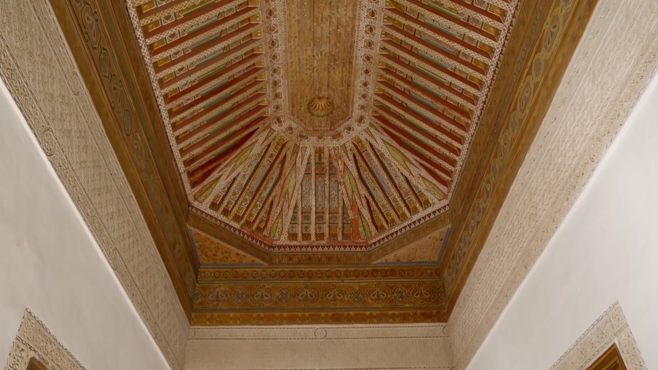Camera tilts down ornate wooden ceiling with geometric patterns in Marrakesh interior