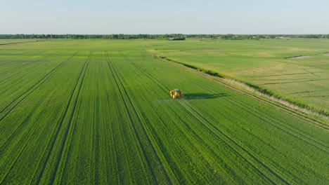 Aerial-establishing-view-of-a-farmer-spraying-crop-fields-with-tractor,-pesticide-and-fertilizer-spraying,-sunny-summer-evening,-golden-hour-light,-wide-drone-shot-moving-forward