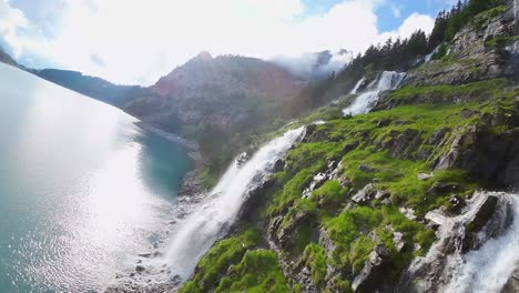 Aerial-flight-next-to-a-beautiful-big-waterfall-on-a-mountain-Landscape,-Drone-Flying-Over-a-Blue-Lake---Oeschinen-Lake,-Switzerland