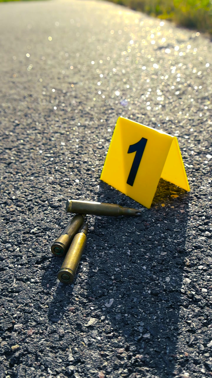 Indicatore di prova giallo numero uno accanto a diversi bossoli trovati su una strada asfaltata, che indica un recente incidente di sparatoria e l'inizio di un'indagine forense della polizia.