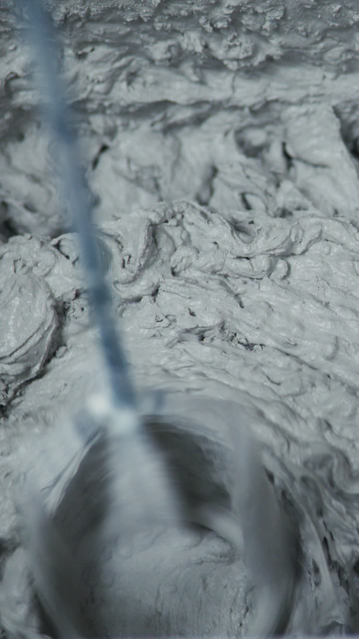 Uno sguardo da vicino al processo di miscelazione di materiale denso e grigio, che mostra l'azione vorticosa e la texture creata dal movimento rotatorio di un mixer