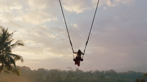 tourist woman swinging over tropical jungle at sunrise travel girl enjoying exotic vacation sitting on swing in having fun holiday lifestyle freedom 4k