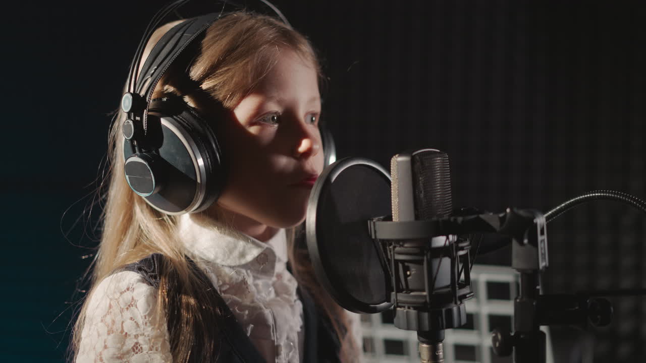 Girl in headphones sings in recording studio. surrounded by soundproof walls. Child demonstrates talent in front of microphone equipped with sound filter
