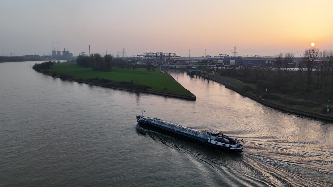Drone vliegt diagonaal naast het schip met zilver-gouden reflecties en de skyline van de loghaven op de achtergrond