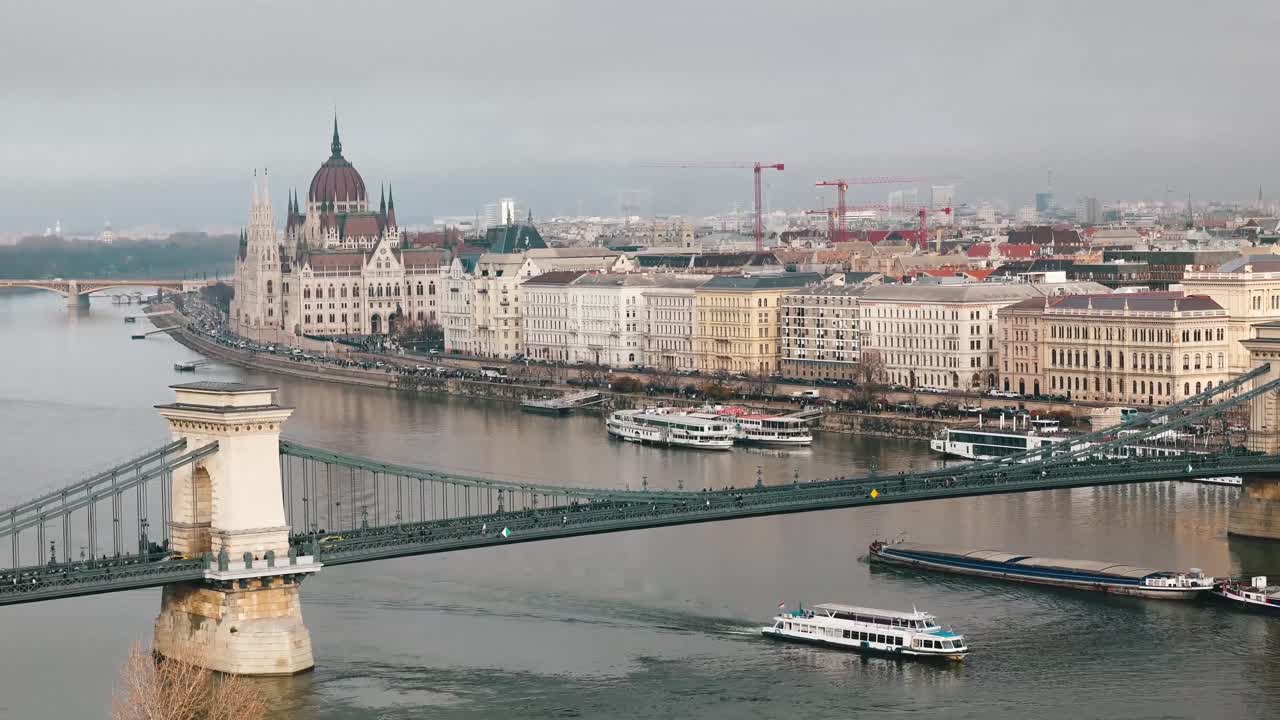 Riprese del Ponte delle Catene Széchenyi, del Palazzo del Parlamento Ungherese e del fiume Danubio. Una nave da crociera e altre navi cargo passano sotto il ponte.