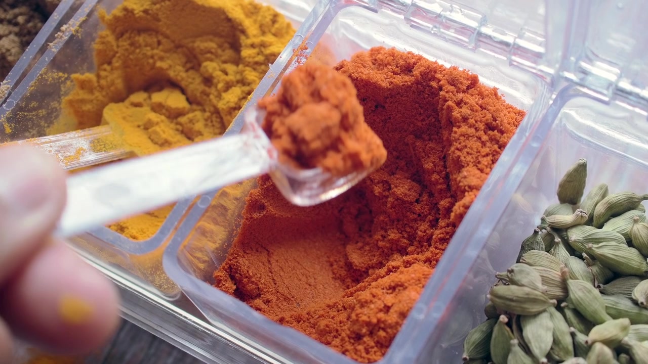 Close-up of Hand Scooping Red Chili Powder from a Spice Container
