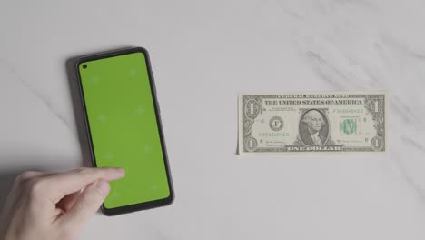 Overhead-Currency-Shot-Of-US-1-Dollar-Bill-Next-To-Person-Using-Green-Screen-Mobile-Phone