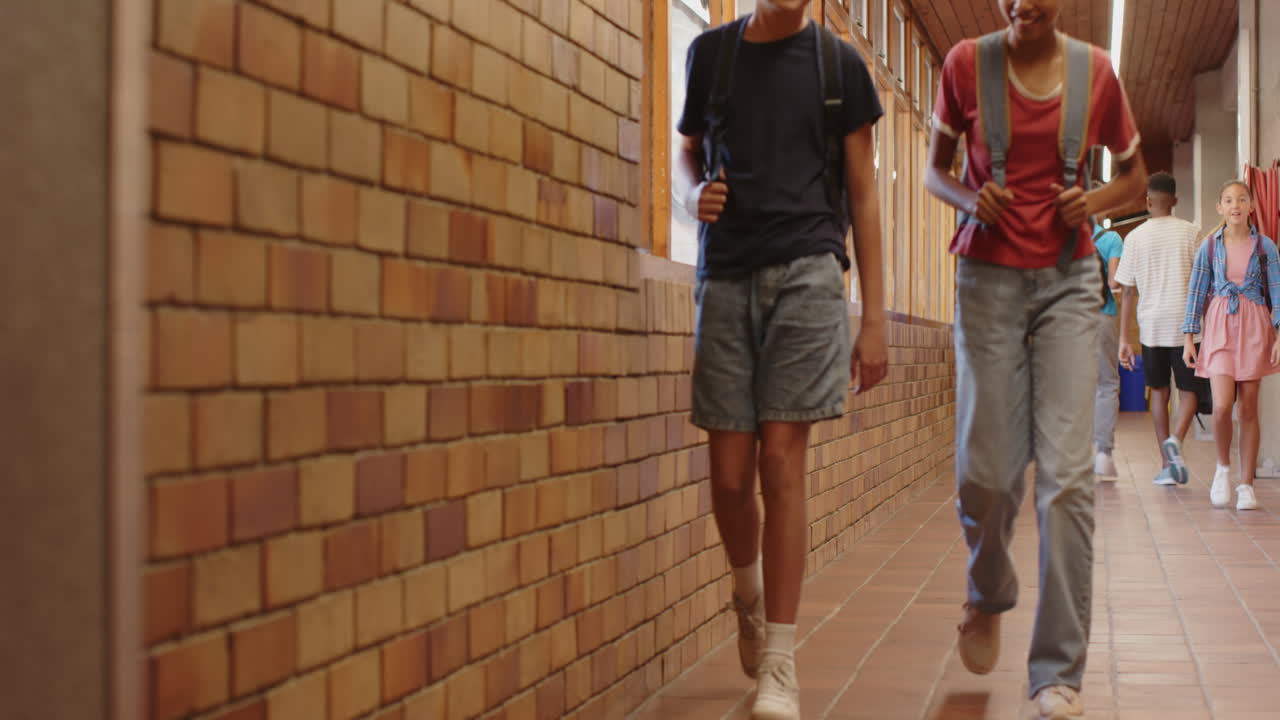 Walking in school hallway, students passing by brick wall, casual attire
