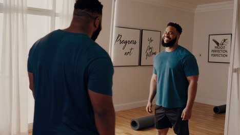 two men in fitness clothes, smiling, inside a home gym.