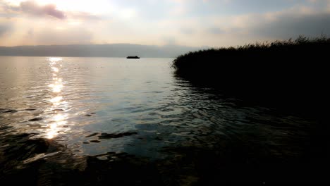 Silhouette-of-a-ship-moving-on-a-calm-lake-toward-cane-and-reed