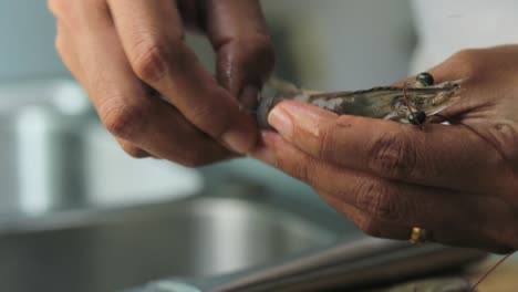 a close up shot of a raw shrimp being peeled by a thai woman in the kitchen