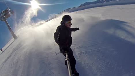 Front-view-of-a-snowboarder-going-down-the-mountain,-making-snow-waves-at-high-speed-with-a-selfie-stick-on-a-clear-day