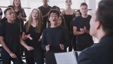 male and female students singing in choir with teacher at performing arts school