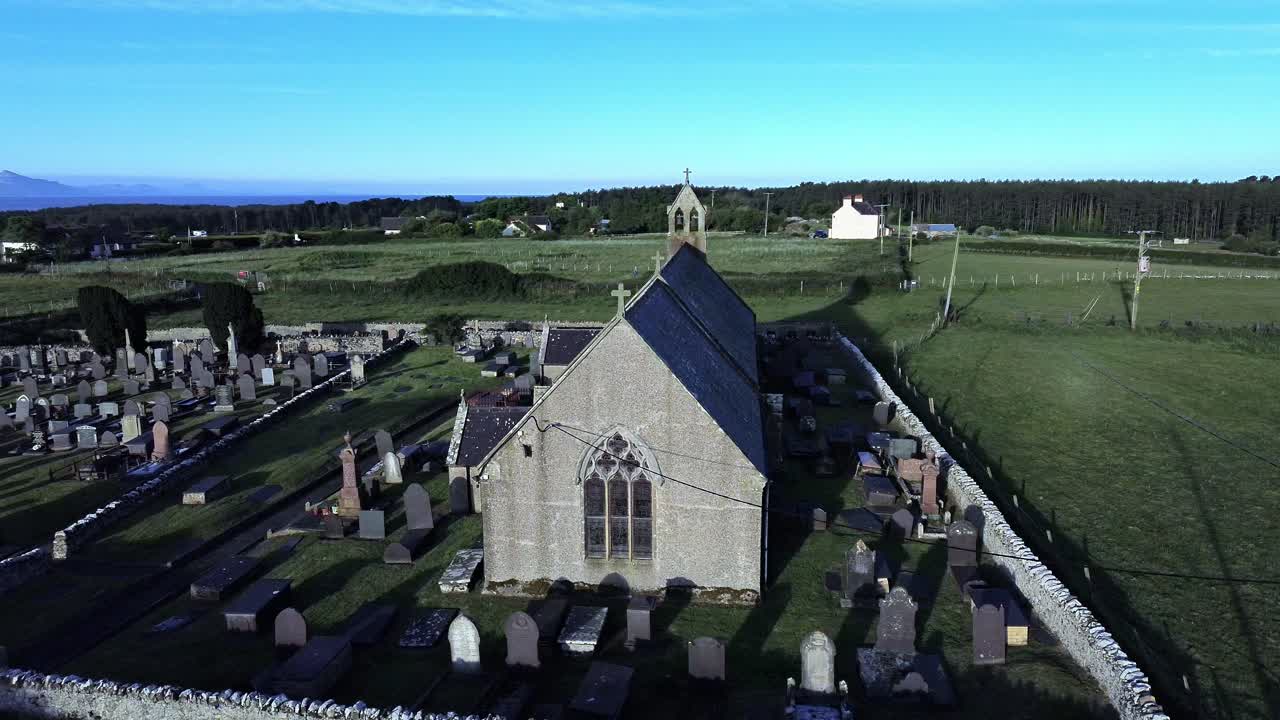 St Peters church in rural Newborough aerial view circling Welsh slate gravestones at sunrise